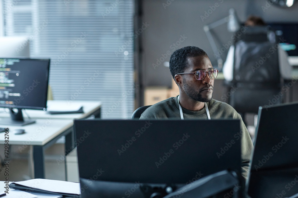 Wall mural portrait of black young man wearing glasses as it programmer using computer and reviewing data in of