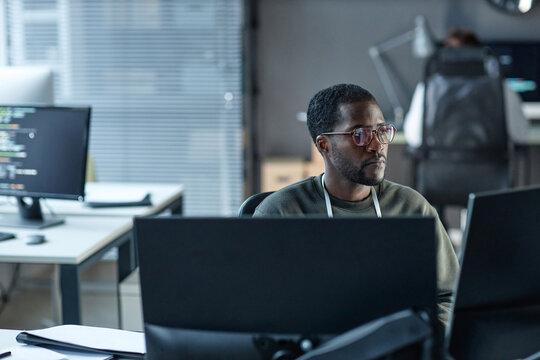 Portrait of Black young man wearing glasses as IT programmer using computer and reviewing data in office copy space