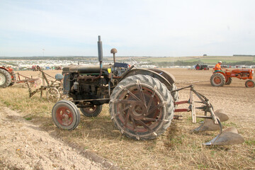  a little historic tractor with a plow closeup at a field with other historic tractors with machinery at a farm event in summer