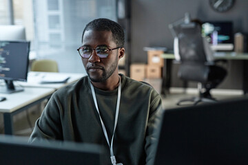 Minimal portrait of focused Black man using computer in IT development office with code lines...