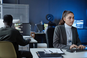 Portrait of young woman using computer in formal IT company office with blue neon light copy space
