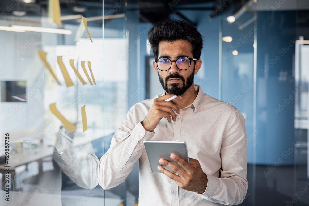 Wall mural Young indian businessman contemplating during office work holding tablet