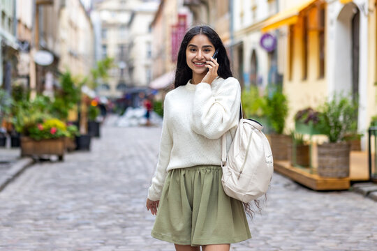 Joyful indian woman enjoying city walk as a tourist with a phone conversation