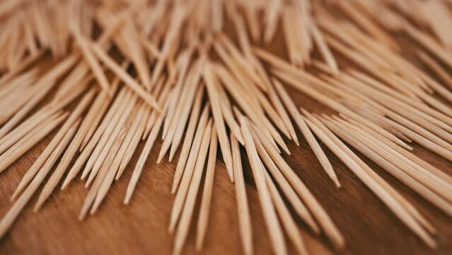 Lots of Scattered Brown Toothpicks Rotate on a Wooden Background. Close up. Top view. Texture of sharp bamboo wooden toothpicks. Home oral care after meals. Teeth cleaning. Blurred motion. Dentistry.