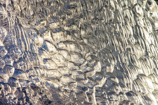 Golden detail of a backlit transparent glacial ice fragment with bubble pattern in Icelnd