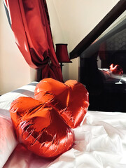 Two red heart-shaped balloons lie on a white bed in a retro bedroom. Decoration for a celebration...