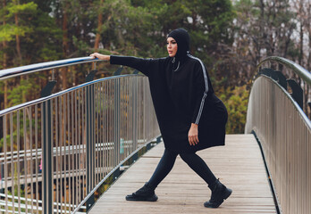 Hijab girl exercising on walkway bridge in early morning. Muslim woman wearing sports clothes doing stretching workout outdoors.