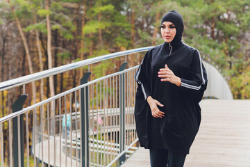 Hijab girl exercising on walkway bridge in early morning. Muslim woman wearing sports clothes doing stretching workout outdoors.