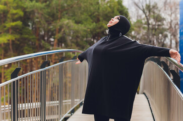 Hijab girl exercising on walkway bridge in early morning. Muslim woman wearing sports clothes doing stretching workout outdoors.