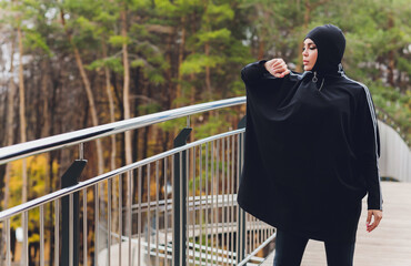 Hijab girl exercising on walkway bridge in early morning. Muslim woman wearing sports clothes doing stretching workout outdoors.
