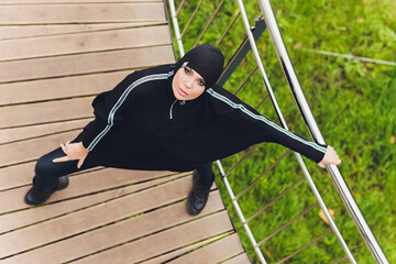 Hijab girl exercising on walkway bridge in early morning. Muslim woman wearing sports clothes doing stretching workout outdoors.