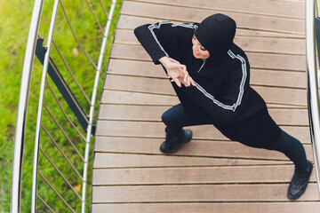 Hijab girl exercising on walkway bridge in early morning. Muslim woman wearing sports clothes doing stretching workout outdoors.