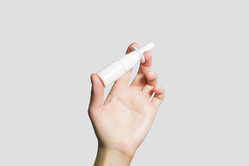 Women's hand holding a white bottle with nasal spray isolated on a grey background