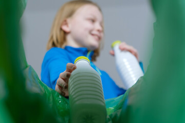 Low angle view a child sorting plastic bottles recycle bin in home. Disposal of milk bottles...