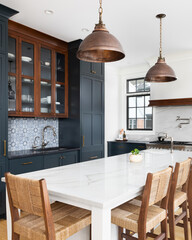 A kitchen detail with blue and wood cabinets with a mosaic tile backsplash, bronze lights over a...