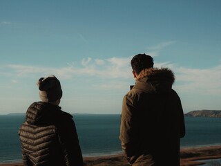 Two persons view the north landscape with the sea and the cliff in the background.