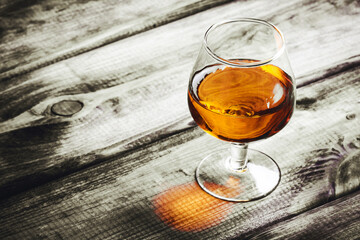 Brandy glass on rustic wood. Cognac alcohol background. Golden liquor closeup. Antique wooden plank...