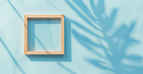 Blank wooden picture frame hanging on blue wall with Palm leaves shadow overlay. Empty poster mockup for art display in sunlight. Minimal interior design. 