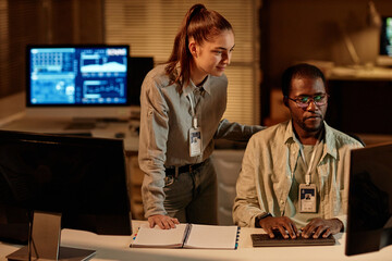 Waist up portrait of two young programmers man and woman looking at computer screen with data in...