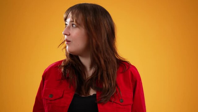Young woman with brown hair wearing red jacket, cover mouth with hands on face say wow omg no way isolated on yellow background studio in slow motion