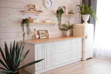 side view of a spacious, bright, cozy kitchen with white furniture and a large window. kitchen with walls decorated with wood and green plants