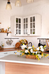 A bouquet of flowers on a wooden table. In the background, the interior of a white kitchen in the Scandinavian style. The concept of home comfort.
