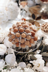 A festive bouquet of nuts on a background of white flowers. Beautifully decorated bouquet of walnuts on a glass plate in the middle of white flowers. Walnut bouquet at a wedding