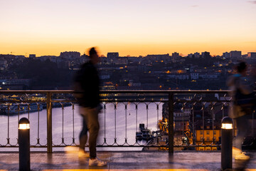 Panoramic view in sunset over the metro deck on the bridge of - D. Luís I - with people looking from behind to the Douro River in the Background. City of Oporto in Portugal.