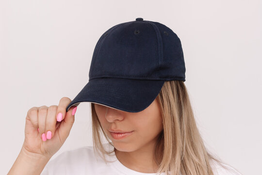 Young caucasian blonde woman holding the visor of the cap showing empty copy space for design or text on a white background - Powered by Adobe