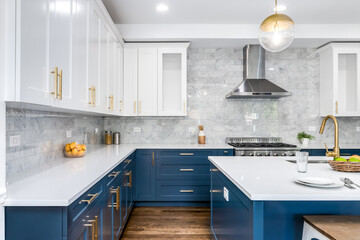 A luxurious white and blue kitchen with gold hardware, stainless steel appliances, marble subway...