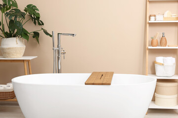 Fototapeta na wymiar Bath tub with wooden board and different personal care products and accessories on shelving unit in bathroom