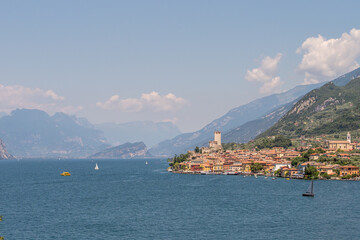 view of boats on the water and houses on the Riva di Guarda coastline, during summer, Italy.