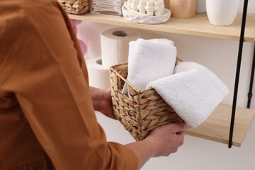 Bath accessories. Woman with basket of clean towels indoors, closeup