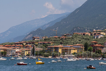 view of boats on the water and houses on the Riva di Guarda coastline, during summer, Italy.