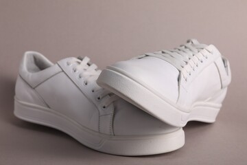 Pair of stylish white sneakers on grey background, closeup