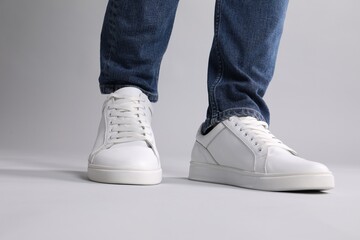 Man wearing stylish white sneakers on grey background, closeup