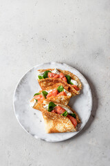 Crepes or thin pancakes with smoked salmon, soft cheese and spinach on a plate top view isolated on gray textured background. Pancake day, Maslenitsa