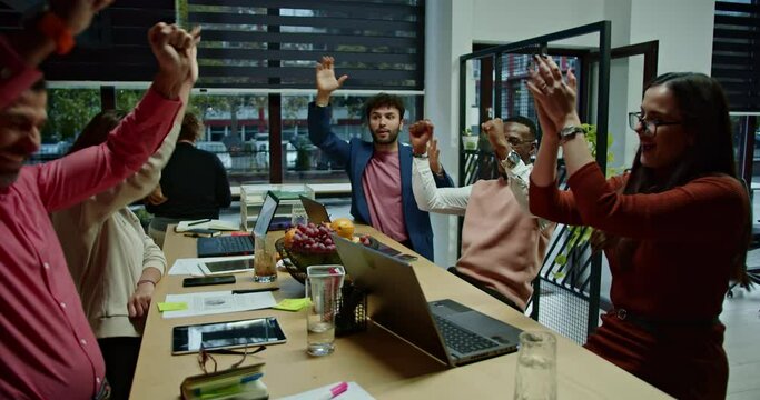 Successful team of multiethnic business partners celebrates with applause in a business setting, showcasing the essence of teamwork and collective achievement.