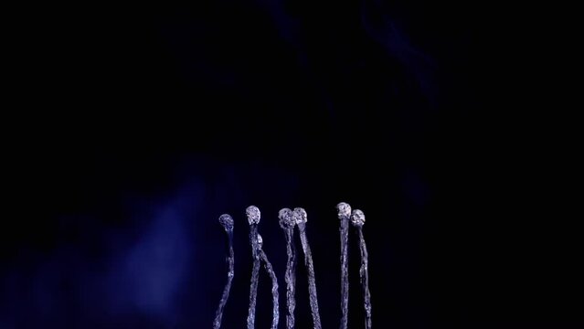 Many Burnt Black Charred Matches Stand in Blue Smoke on a Black Background. Empty Space. Burnt Matchsticks. Texture. A row of matches, burning sulfur heads. Blurred motion. Macro. Slow motion. End.
