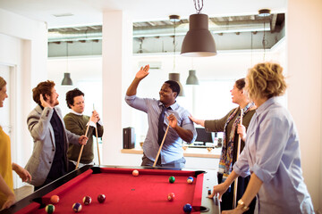 Group of coworkers playing pool and celebrating in a modern office break room