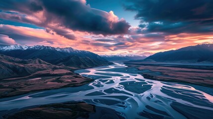  a river flowing through a lush green valley under a sky filled with lots of clouds and snow covered mountains under a purple and blue sky filled with white fluffy clouds.