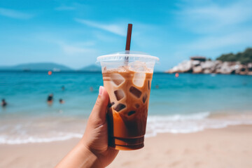 Person hand holding plastic glass with iced coffee against background of landscape with blue sea, refreshing summer drink with ice - Powered by Adobe