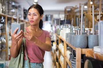 Adult Asian woman choosing soap dispencer in housewares store.