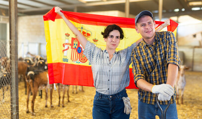 Cheerful biracial couple of farmers, engaged in breeding of domestic goats, standing in goat shed...