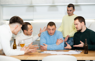 Troubled man reading legal notice surrounded by friends providing moral support sitting at table n...