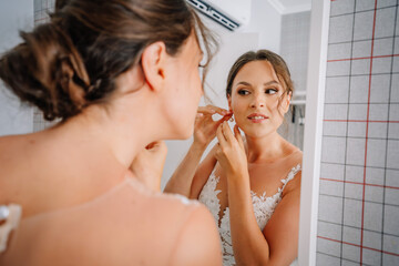 Valmiera, Latvia - July 7, 2023 - A bride in a lace dress is putting on her earring while looking at her reflection in a mirror.