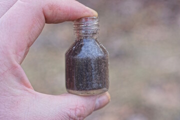 fingers holding one small old gray glass bottle on the street