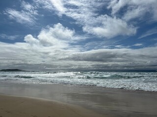 Cloudy sky filtering light onto waves breaking onto a beach.