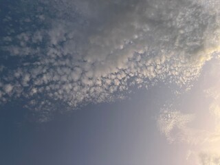 Naklejka na ściany i meble Light on cotton ball puffy clouds an evening sky.