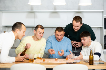 Friends drinking beer and enthusiastically playing a board game at home